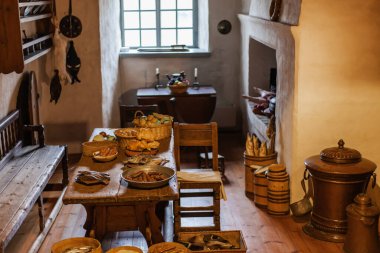 Ahşap bir masanın üzerinde ortaçağ yemekleri sergilenen eski bir şato mutfağı. Tarihi atmosfer, miras sergisi için antika dekorlar, çömlekçilik ve sahte yiyeceklerle yeniden canlandırıldı..
