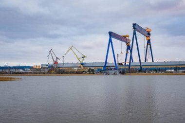 Denize yakın bir tersanede inşa edilen büyük bir geminin fotoğrafı, uzak bir noktadan çekildi. Vinçleri, iskeleyi, büyük gemi yapısını ve endüstriyel deniz ortamını gösterir.