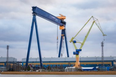 Denize yakın bir tersanede inşa edilen büyük bir geminin fotoğrafı, uzak bir noktadan çekildi. Vinçleri, iskeleyi, büyük gemi yapısını ve endüstriyel deniz ortamını gösterir.