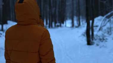 4K videosunda bir adam kış ormanında dikiliyor, arkasına bakıyor ve yavaşça kameraya doğru dönüyor. Sahne atmosferik ve sinematik, alçak ışık, karla kaplı ağaçlar ve sakin bir kış havası var..