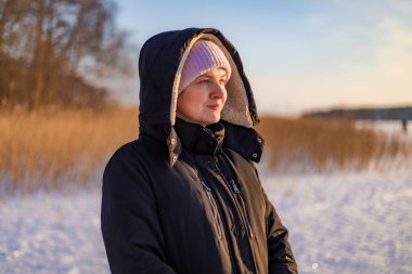 Siyah ceketli bir kadın bir kış günü donmuş bir deniz gölünün kıyısında duruyor ve uzaklığa bakıyor..