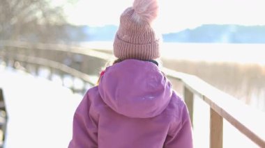 Kışın küçük bir köprüde yürüyen bir çocuğun 4K videosu. Karla kaplı çevre ve soğuk mevsimsel atmosfer sakin ve manzaralı bir kış anı yaratır. Sahne çocukluk keşiflerini, bağımsızlığı ve sessiz açık hava aktivitelerini simgeliyor..