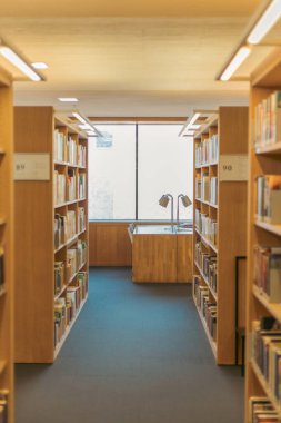 Sıralar dolusu kitap rafları kütüphane koridorunda sıcak ve davetkar bir atmosfer yaratıyor. Arka plan hafifçe bulanık ve bulanık....