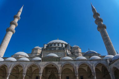 İstanbul, Türkiye 'deki Osmanlı İmparatorluk Camii' nin görkemli Sleymaniye Camii 'nin alçak açılı bir görüntüsü. Avlunun manzarası ana kubbesini, yarım kubbesini ve açık mavi gökyüzünün altında iki minaresini gösteriyor.. 