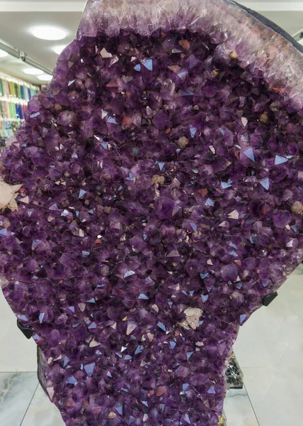 Büyük bir ametist jeotunun yakın plan görüntüsü, parlak yüzlü sayısız canlı mor kristal sergiliyor. Doğal ham taş oluşumu çerçeveyi doldurur, mineralin zengin rengini ve karmaşık yapısını vurgular..