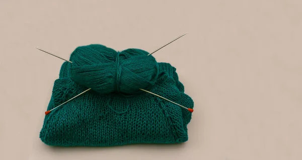 Tarafsız bir zemin üzerinde örgü iğneleri olan yeşil merino yününden örülmüş bir öğe, örgü dersleri, el işi ilhamı ve sosyal medya içeriği için mükemmel.