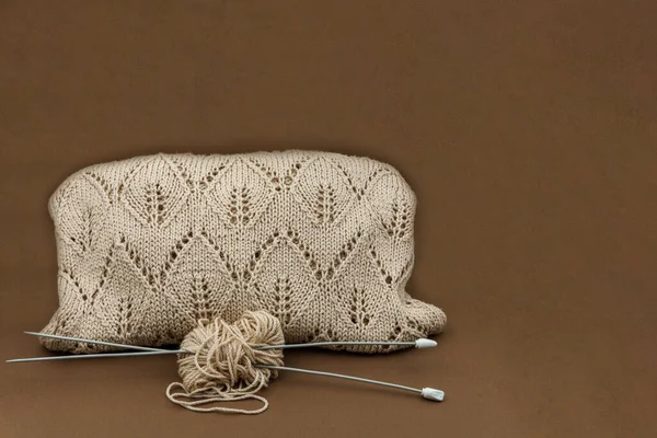 Kahverengi arka planda örgü iğneleriyle pamuk ipliğine örülmüş öğe, örgü dersleri, el sanatları ilhamı ve sosyal medya içeriği için mükemmel.