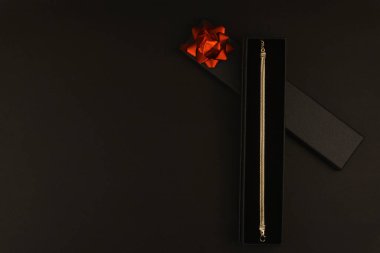 Siyah bir hediye kutusunda sunulan zarif altın bilezik. Koyu arkaplan, metin veya markalaşma için alanı olan sofistike bir atmosfer yaratır..