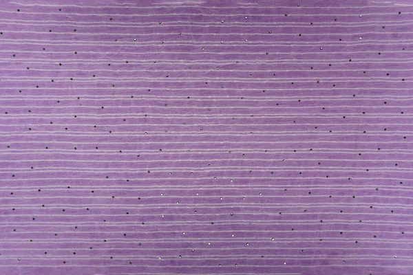 Düz olmayan bir yatay çizgi yapısı ve küçük, dağınık yapay elmaslı süslemeleri olan leylak ya da lavanta rengi ipek bir yüzeye yakın plan. Hassas moda ya da gece kıyafeti için arka plan