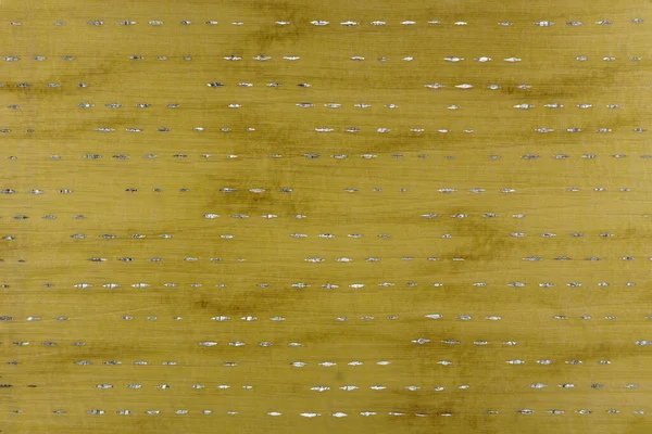 Açık ipek bir tekstilin yakın çekimi. Limon, zeytin ve hardal tonlarında küçük parlak eşkenar şekilli yatay çizgilerle süslenmiş soyut benekli bir arkaplan.