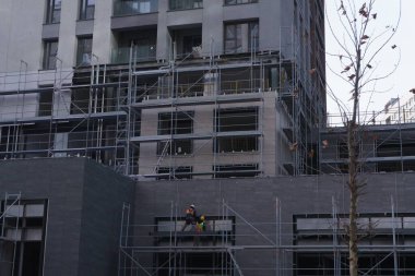 Güvenlik yelekleri içinde inşaat işçileri modern iskan gökdelenine ön cephe kuruyorlar.