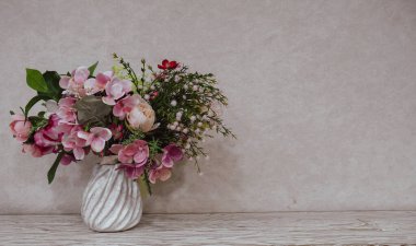 Seramik bir vazoda pembe ve pastel çiçeklerle süslü zarif bir çiçek aranjmanı var. Ahşap bir yüzeye, yumuşak, nötr bir arkaplana yerleştirilmiş. Minimalist ev dekorasyonu, romantik ruh hali, doğal ışık, metin için kopya alanı, iç tasarım