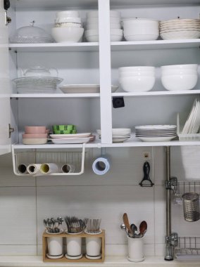 Temiz mutfak tezgahının üzerinde düzgün düzenlenmiş tabak, tabak ve kâseler ve çatal bıçak ve çatal bıçaklarla dolu beyaz mutfak dolabını aç. Minimalist mutfak iç mimarisi, ev organizasyonu ve depolama konsepti, düzenli modern ev halkı.