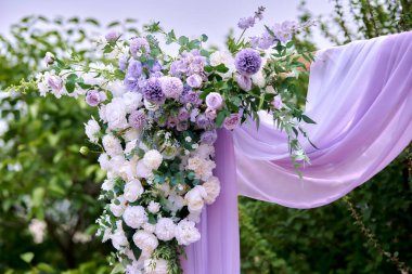 Çiçekler ve kumaşla süslenmiş romantik açık hava düğün kemeri.