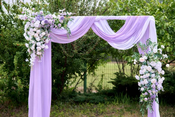 Çiçekler ve kumaşla süslenmiş romantik açık hava düğün kemeri.