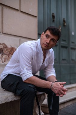 İtalya, Roma 'da taştan bir bankta oturan beyaz gömlekli ve siyah pantolonlu bir adamın portresi..