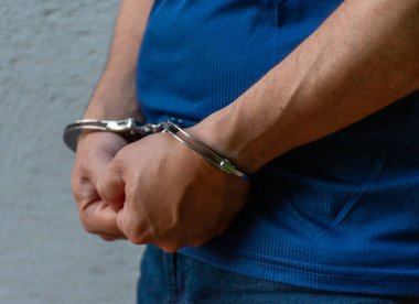 Duvara dayanan metal kelepçeli erkeklerin yan görüntüsü. Hapis, gözaltı ve adalet sembolü.