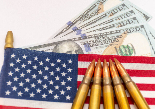 Several rifle bullets placed on a small United States flag with hundred dollar banknotes, symbolizing power, finance, and conflict.