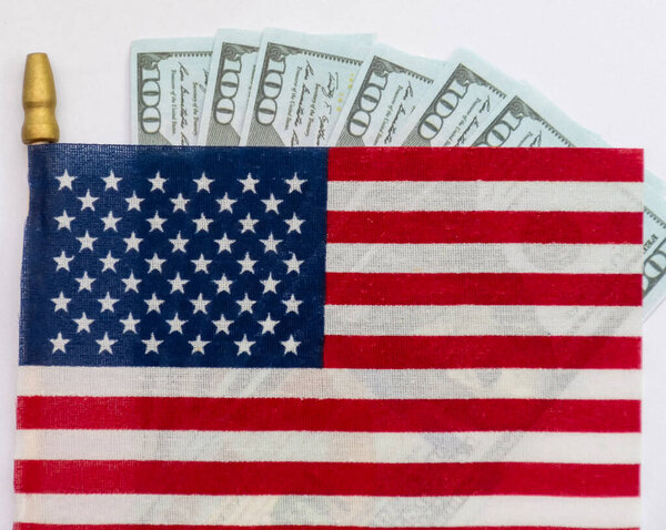 Several rifle bullets placed on a small United States flag with hundred dollar banknotes, symbolizing power, finance, and conflict.