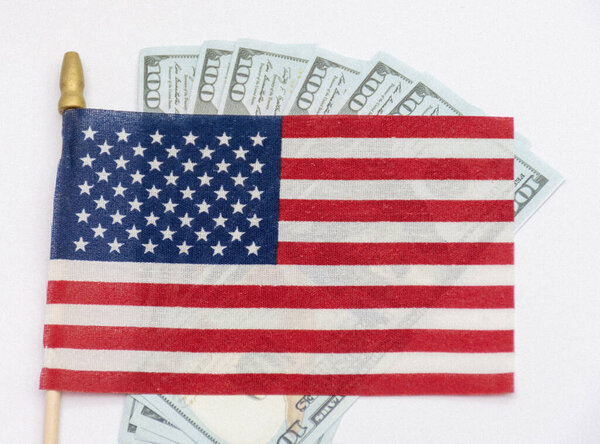 Several rifle bullets placed on a small United States flag with hundred dollar banknotes, symbolizing power, finance, and conflict.