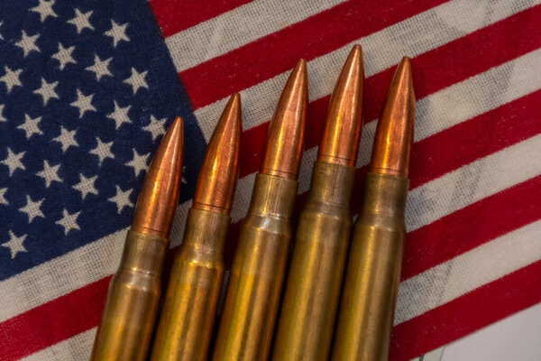 Several rifle bullets placed on a small United States flag with hundred dollar banknotes, symbolizing power, finance, and conflict.