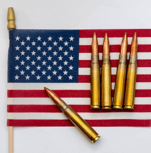 Several rifle bullets placed on a small United States flag with hundred dollar banknotes, symbolizing power, finance, and conflict.