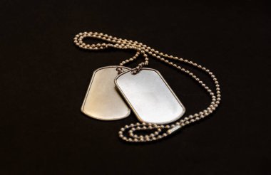 Siyah yüzeyde duran ve askerlik, kimlik ve anıları sembolize eden bir çift boş metal künye..