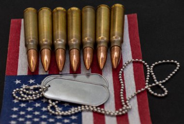 Tüfek fişeklerini ve Amerikan bayrağına yerleştirilmiş gümüş askeri künyeleri kapatın. Hizmet, cesaret ve özgürlüğün savunmasını temsil ediyor..