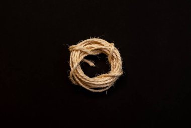Küçük bir düğümle bağlanmış ve dayanıklılığı, birliği ve el yapımı çalışmayı temsil eden koyu arkaplana yerleştirilmiş doğal kıvrımlı bir ip..