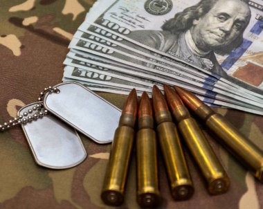 Metal künyeleri, tüfek mermilerini kapatın ve askeri harcamaları, savaş ekonomisini ve savunma finansmanını temsil eden kamuflaj geçmişine 100 dolarlık banknotlar yerleştirin..