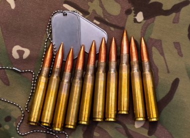 Askeri kimliği, savunması, fedakarlığı ve muharebe hazırlığını simgeleyen pirinç tüfek fişeklerini ve kamuflajlı tekstil üzerindeki gümüş askeri künyeleri kapatın..