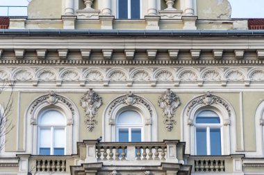 Tarihi bir binanın dış cephesi sıva elementleri, kemerli pencereler ve dekoratif süslemelerle süslenmiş..