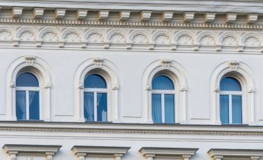 Kemerli pencereleri, dekoratif pervazları ve klasik mimari unsurları olan tarihi bir binanın cephesi..