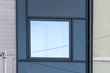 Karanlık metal panelleri, kıvrımlı kaplamaları ve minimalist cephe tasarımı olan modern bir binanın penceresi..