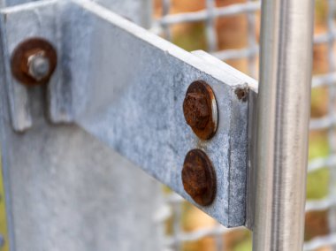 Çitin üzerindeki metal cıvatalar paslı ve görünür yapısal elementlerle yakın plan..