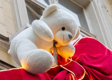 Kırmızı kumaşlı ve sıcak dekoratif ışıklandırmalı bir vitrinde büyük beyaz bir oyuncak ayı..