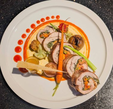Elegant gourmet chicken roulade stuffed with fresh spinach, carrots, and peppers, beautifully plated with roasted vegetables and vibrant sauce drops.