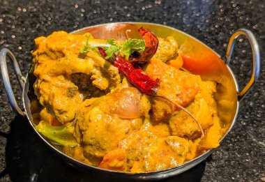 Rich and flavorful chicken curry served in a hammered copper bowl, topped with roasted chili and herbs.