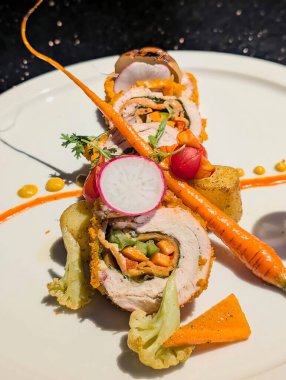 Elegant gourmet chicken roulade stuffed with fresh spinach, carrots, and peppers, beautifully plated with roasted vegetables and vibrant sauce drops.