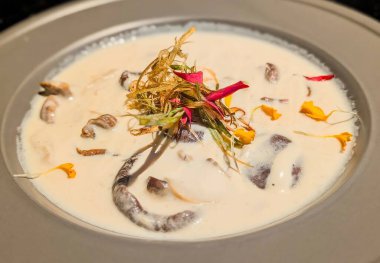 Close-up of a creamy Thai soup served in a black bowl, topped with colorful bell peppers, fresh herbs, and red chili garnish.
