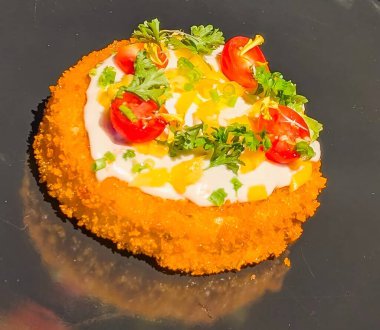 A beautifully plated crispy breaded appetizer topped with creamy sauce, diced yellow peppers, cherry tomatoes, and fresh herbs.