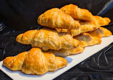 Freshly baked chocolate puff pastries stacked on a dark surface. The golden, flaky layers and rich chocolate filling create a warm, appetizing presentation.