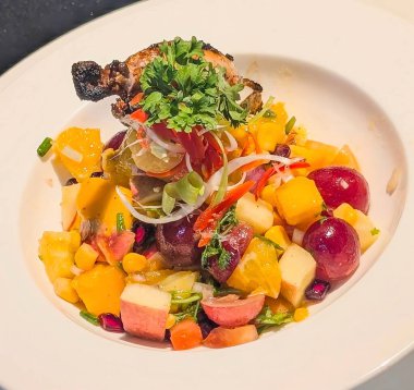 Juicy grilled chicken leg served with a colorful fruit and vegetable salad made of mango, grapes, corn, and herbs. A vibrant, healthy gourmet meal with elegant restaurant-style presentation
