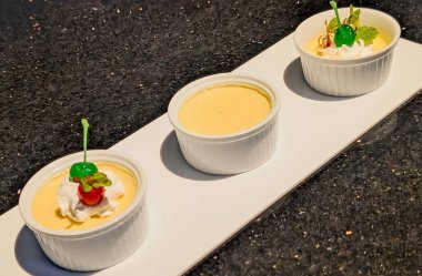 Description: Elegant vanilla custard served in a white ramekin, topped with whipped cream and colorful glazed cherries.