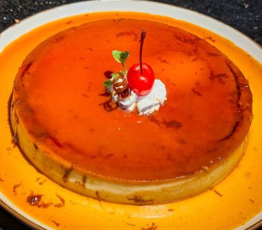 Close-up of a smooth caramel flan topped with whipped cream,red cherry,and mint leaves.The golden caramel glaze and glossy texture make this classic dessert perfect for illustrating bakery products.