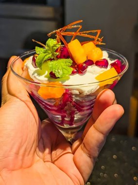Beautifully arranged assorted fruit custard desserts served in elegant glasses, topped with cherries, wafer rolls, mint leaves, and vibrant mixed fruits.A delicious, colorful, and creamy sweet treat.