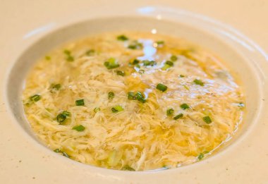 Close-up of traditional Chinese egg drop soup garnished with chopped green onions. Light, comforting, and flavorful Asian appetizer served in a bowl, perfect for illustrating homemade cuisine.