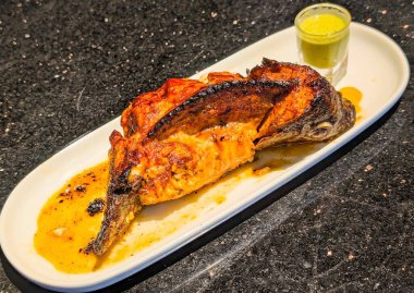 Close-up of spicy garlic chicken coated in rich chili sauce, garnished with red chili, garlic, and cucumber slices.