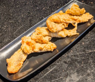 Crispy deep-fried squid tempura served on a dark plate, showcasing a golden-brown texture and light, airy batter. A delicious seafood appetizer perfect for gourmet dining or restaurant menus.