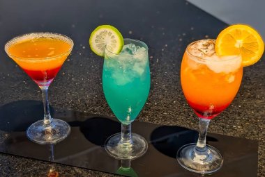 A vibrant trio of refreshing mocktails in shades of orange, blue, and red served on a glossy surface. Each drink is garnished with fresh citrus slices, showcasing a perfect mix of tropical colors.